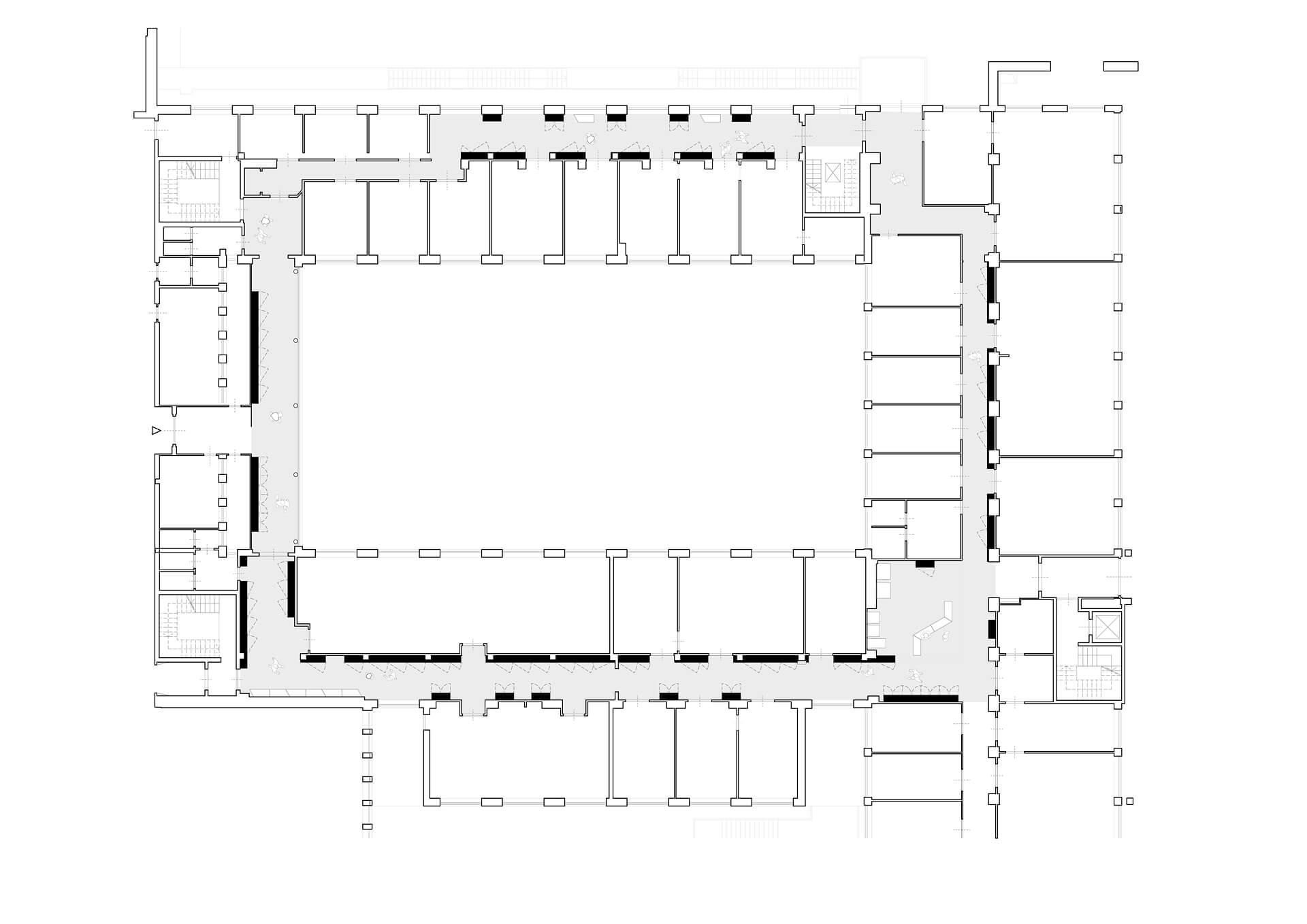 Pianta architettonica del piano dell’edificio oggetto di intervento, rappresentata mediante disegno tecnico in scala, utilizzato come base per la progettazione dell’allestimento museale. La tavola mostra un impianto a corte con grande spazio centrale rettangolare circondato da ambienti perimetrali distribuiti lungo tutti i lati, collegati da un sistema continuo di corridoi e aperture. Il disegno evidenzia la struttura muraria esistente, i pilastri, le partizioni interne e i principali collegamenti verticali, tra cui scale e vani di distribuzione, consentendo di leggere l’organizzazione funzionale dell’edificio. Le campiture più scure lungo alcune pareti indicano le porzioni interessate dall’intervento espositivo, dove sono inseriti i nuovi elementi di allestimento, pannellature e sistemi espositivi integrati. L’ampio spazio centrale, lasciato libero, funge da fulcro distributivo e da area di relazione tra i diversi ambienti, mentre le sale lungo il perimetro ospitano il percorso museale articolato in sequenze tematiche. La pianta documenta la fase di coordinamento tra architettura esistente e progetto di allestimento, utile per definire il posizionamento degli arredi, dei supporti espositivi e degli impianti, garantendo continuità del percorso e leggibilità degli spazi. L’immagine costituisce quindi un elaborato di progetto utilizzato per lo studio della distribuzione funzionale e per l’integrazione tra struttura storica dell’edificio e nuovo sistema museografico.