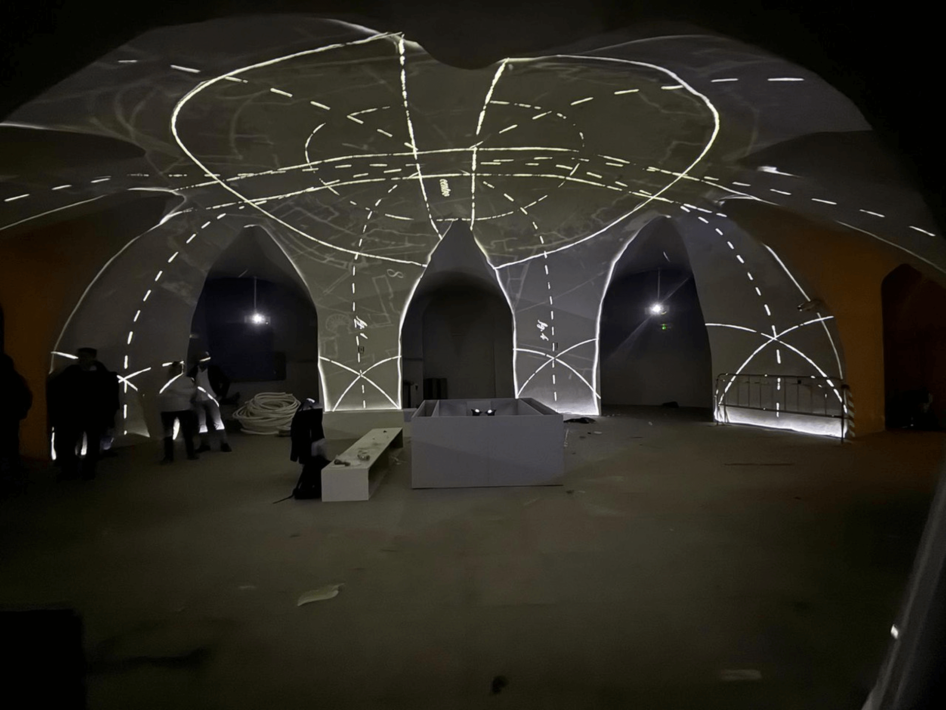 Sala con volte a crociera illuminate da una proiezione luminosa che disegna linee e schemi geometrici sulle superfici architettoniche.
