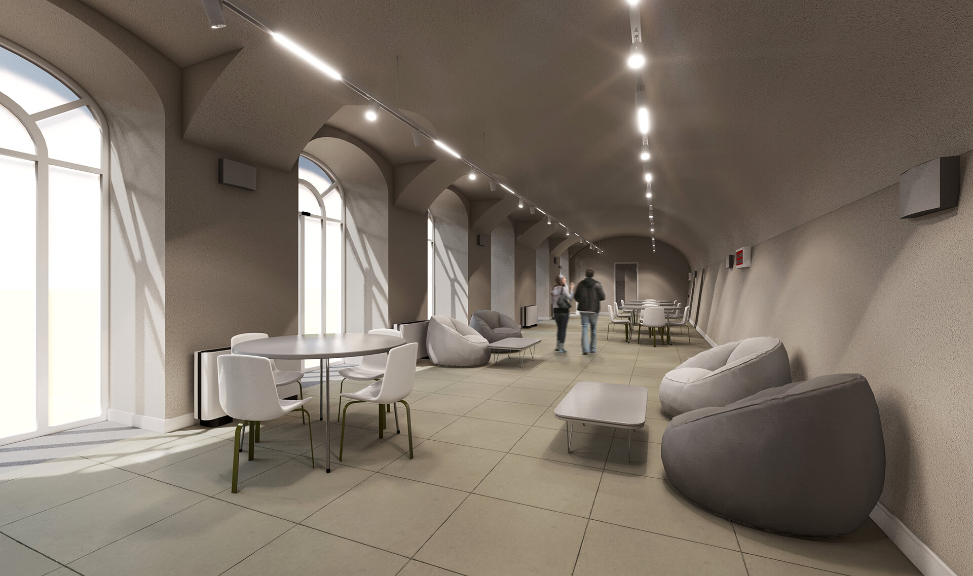 L'immagine mostra un ambiente interno moderno e ben illuminato, con un'atmosfera accogliente e funzionale. Si tratta di uno spazio dalle caratteristiche architettoniche distintive, come gli archi a tutto sesto e le ampie finestre che lasciano entrare molta luce naturale, creando un ambiente luminoso. Le pareti sono di un colore neutro, che aggiunge una sensazione di ampiezza all'area. Dettagli principali dell'ambiente: Arredi: Ci sono poltrone morbide e sedie moderne in metallo, che conferiscono un aspetto contemporaneo e comodo all'ambiente. Le poltrone a sacco, in particolare, sono l'elemento che aggiunge un tocco di informalità, suggerendo che l'ambiente possa essere adibito ad uno spazio di socializzazione, relax o studio. Illuminazione: La luce è diffusa uniformemente grazie ai faretti a soffitto, che mettono in risalto l'altezza e le curve del soffitto. L'illuminazione è posizionata in modo strategico lungo il soffitto, senza oscurare la vista esterna dalle finestre. Spazio: Il pavimento è piastrellato con piastrelle di grande formato, che contribuiscono a rendere l'ambiente arioso e moderno. L'ampio spazio consente un flusso libero di movimento, con tavoli e sedie disposti in modo funzionale ma informale. In generale, l'ambiente trasmette un senso di modernità, apertura e comfort, suggerendo che lo spazio possa essere utilizzato per attività collettive o come area comune all'interno di un edificio pubblico o di un centro di studio.