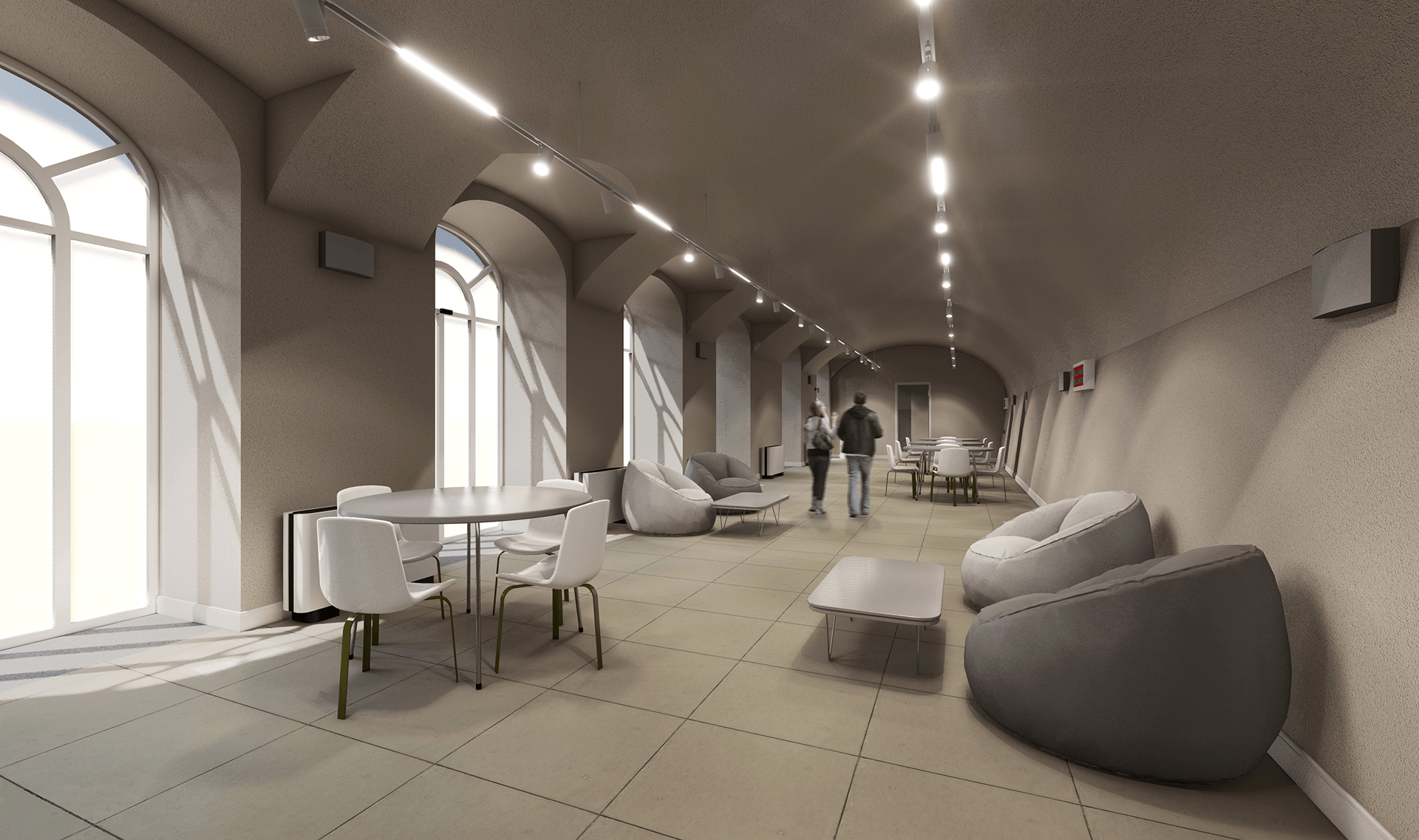 L'immagine mostra un ambiente interno moderno e ben illuminato, con un'atmosfera accogliente e funzionale. Si tratta di uno spazio dalle caratteristiche architettoniche distintive, come gli archi a tutto sesto e le ampie finestre che lasciano entrare molta luce naturale, creando un ambiente luminoso. Le pareti sono di un colore neutro, che aggiunge una sensazione di ampiezza all'area. Dettagli principali dell'ambiente: Arredi: Ci sono poltrone morbide e sedie moderne in metallo, che conferiscono un aspetto contemporaneo e comodo all'ambiente. Le poltrone a sacco, in particolare, sono l'elemento che aggiunge un tocco di informalità, suggerendo che l'ambiente possa essere adibito ad uno spazio di socializzazione, relax o studio. Illuminazione: La luce è diffusa uniformemente grazie ai faretti a soffitto, che mettono in risalto l'altezza e le curve del soffitto. L'illuminazione è posizionata in modo strategico lungo il soffitto, senza oscurare la vista esterna dalle finestre. Spazio: Il pavimento è piastrellato con piastrelle di grande formato, che contribuiscono a rendere l'ambiente arioso e moderno. L'ampio spazio consente un flusso libero di movimento, con tavoli e sedie disposti in modo funzionale ma informale. In generale, l'ambiente trasmette un senso di modernità, apertura e comfort, suggerendo che lo spazio possa essere utilizzato per attività collettive o come area comune all'interno di un edificio pubblico o di un centro di studio.